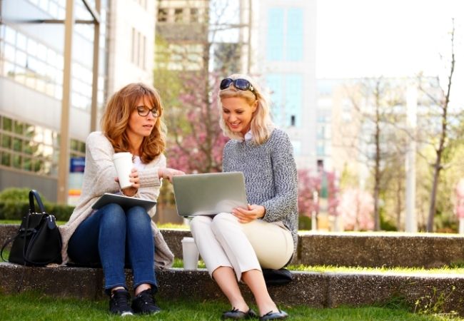 Zwei Frauen sitzen auf einer Mauer und besprechen anhand eines Laptops das Business Profiling